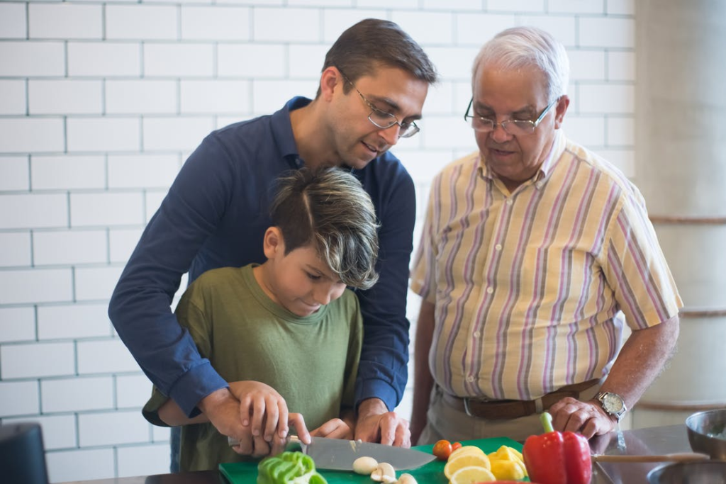A man, his son, and his senior father cutting vegetables together.