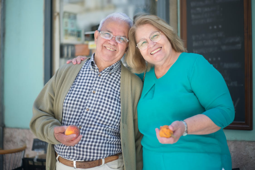 Older adults holding fruits and smiling at the camera.