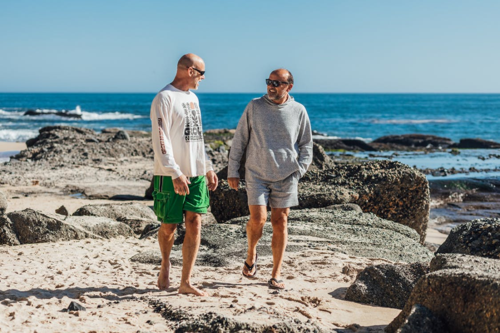 A man and his senior father walking on the beach.