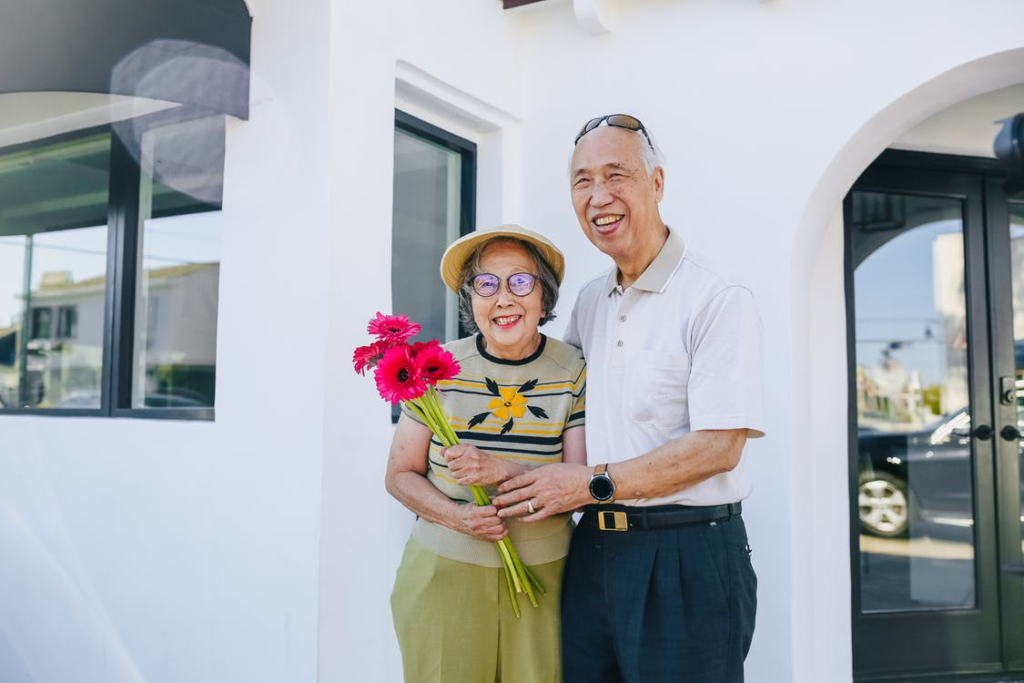 A senior couple smiling while holding flowers.