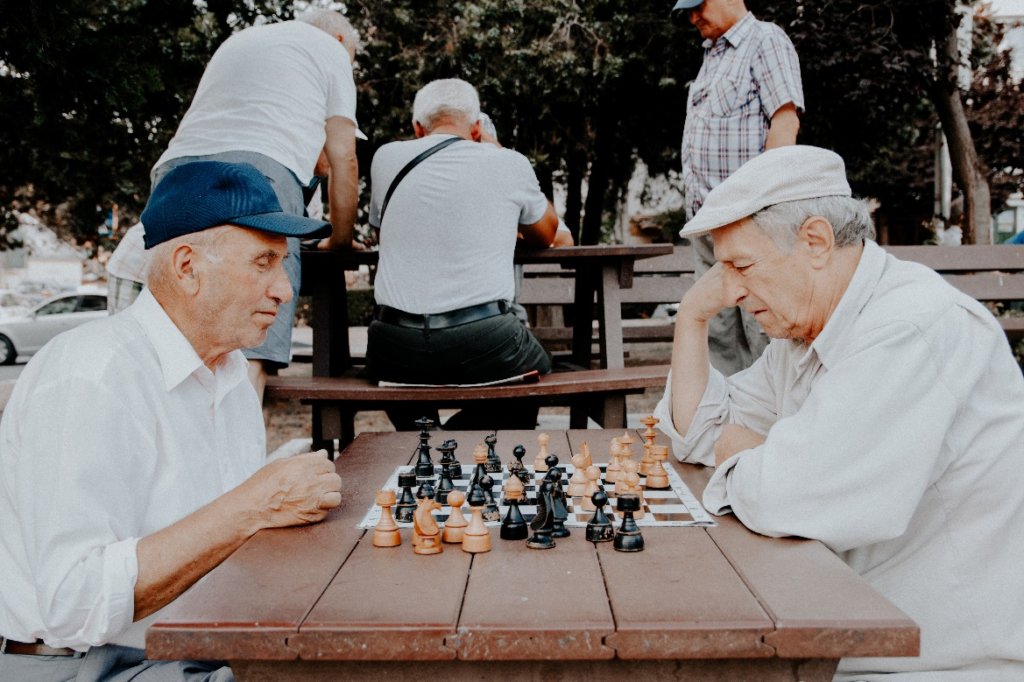Two men playing a game of chess on a bench. 