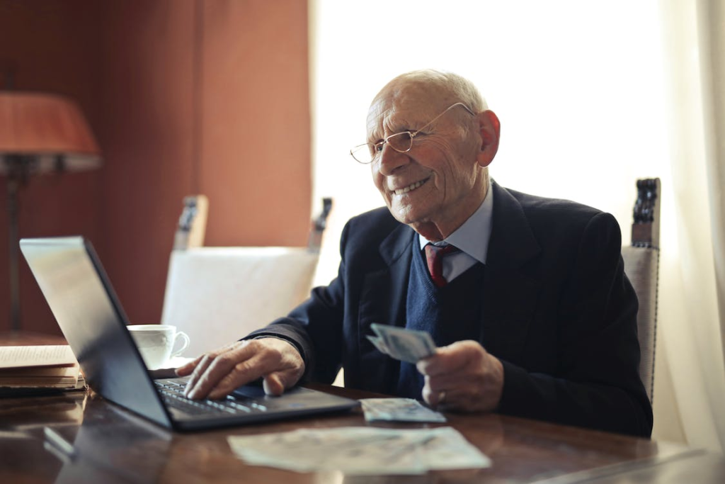 A senior working on a laptop and holding banknotes