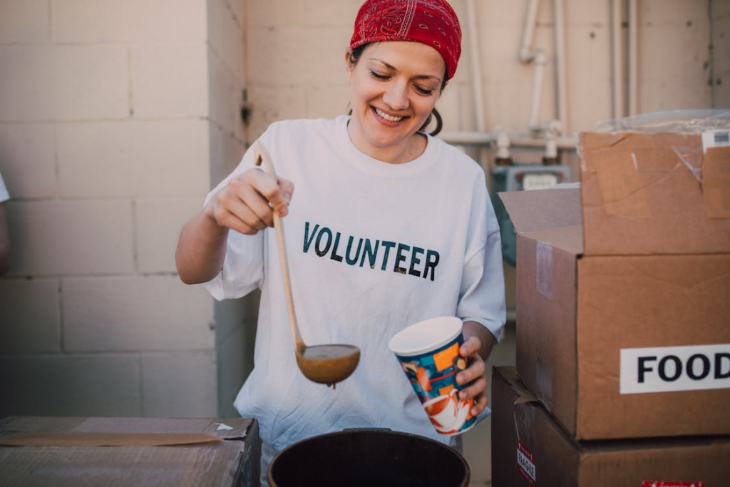 A person wearing a volunteer shirt while pouring soup into a cup